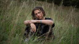 Person wearing all black sitting in a field with their arms resting on their knees.